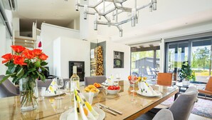 Een moderne eetruimte met een glazen tafel gedekt voor een maaltijd, omringd door comfortabele zitplaatsen en uitzicht op het buitengebied.
