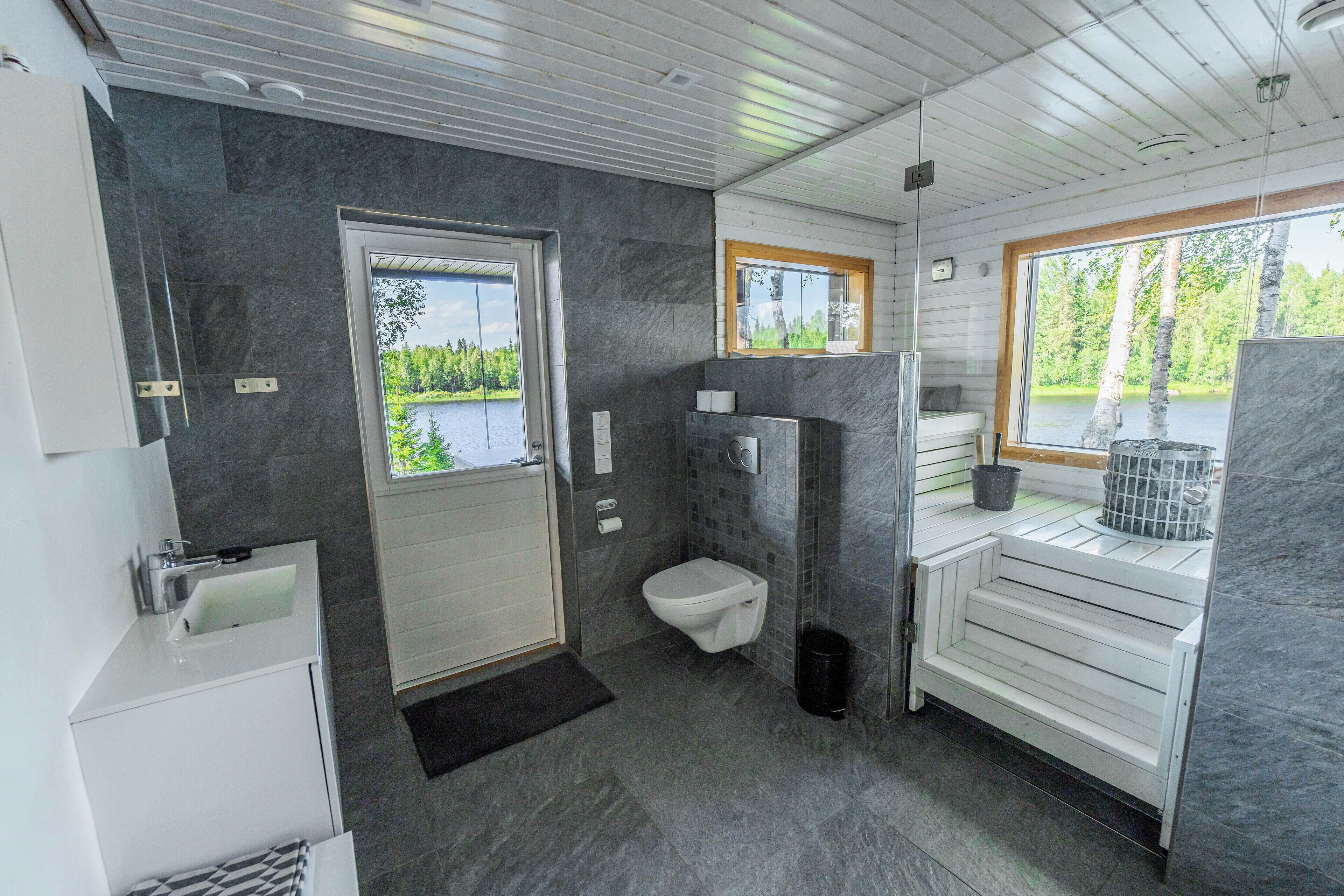A modern bathroom with a toilet, sink, and shower area. There is a window providing a view of the outdoors.