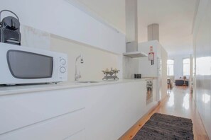A modern kitchen with white cabinetry, a microwave, a kettle, and a coffee maker.