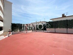 A red-tiled rooftop with a white building and a green hedge in the background. - 1st line beach flat - Edif. Olimpic  (Cambrils)
