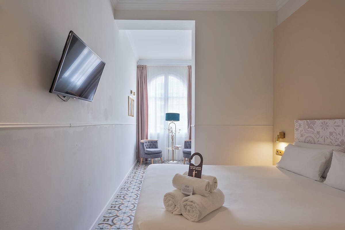 A hotel room with a bed, a TV mounted on the wall, a chair, a desk, and a sign indicating the room is for guests.