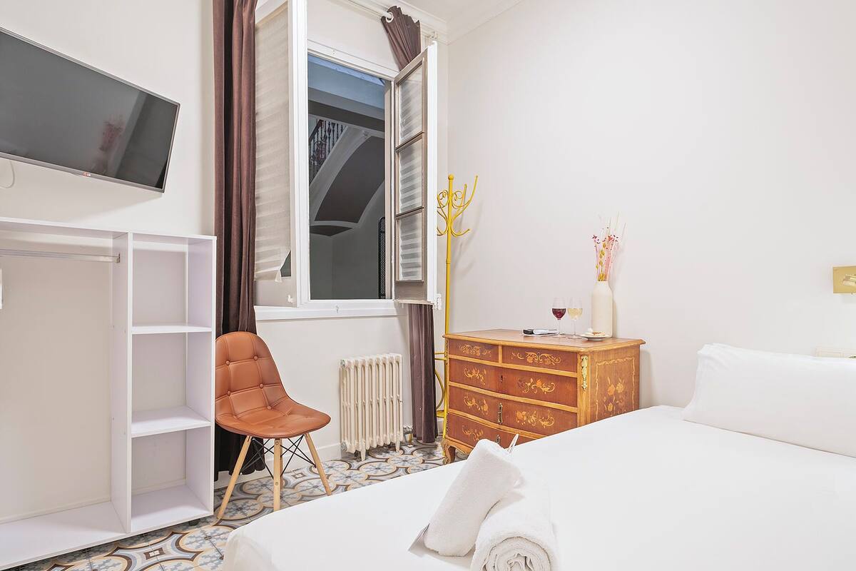 A hotel room with a bed, a chair, a dresser, a radiator, and a television mounted on the wall.