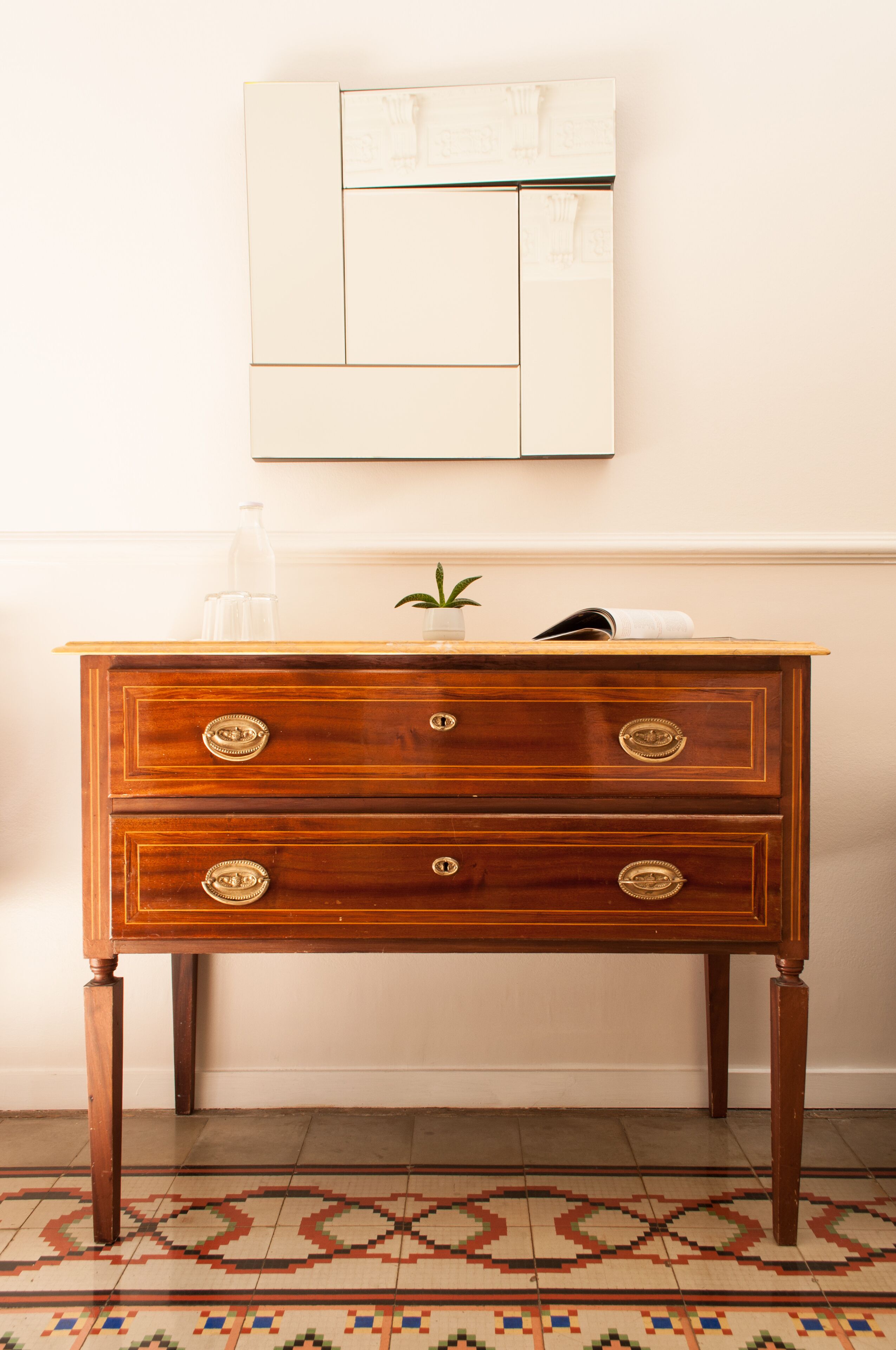 A wooden dresser with drawers, a small plant, and a glass on top.