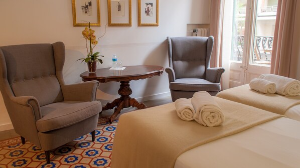 A hotel room with two armchairs, a round wooden table with a potted orchid, a bed with rolled towels, and a patterned floor. - Mihlton Barcelona Boutique B&B (Barcelona)