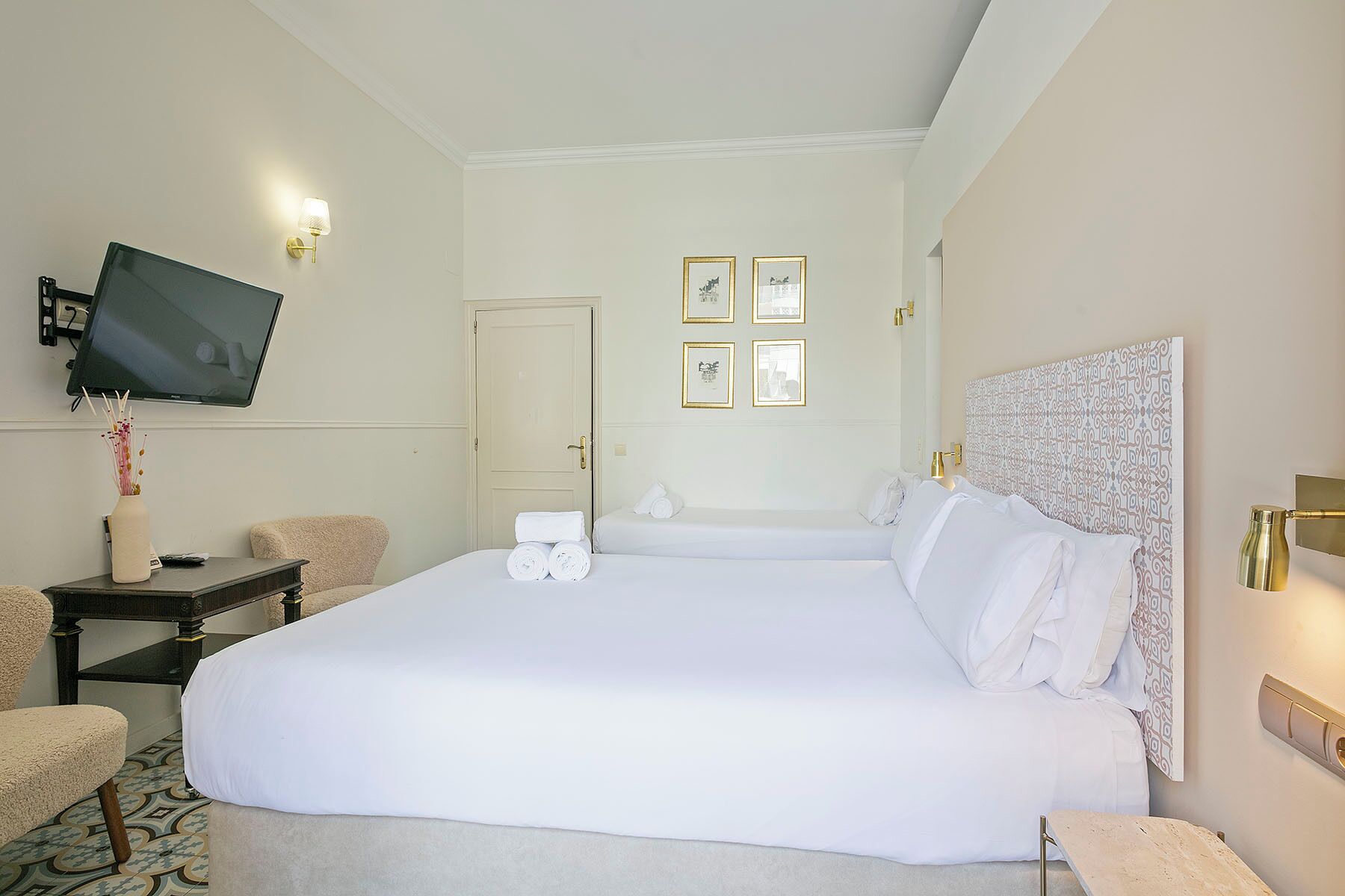 Habitación de hotel con una cama grande, un televisor de pantalla plana en la pared, una mesita de noche con lámpara y una puerta con espejo.