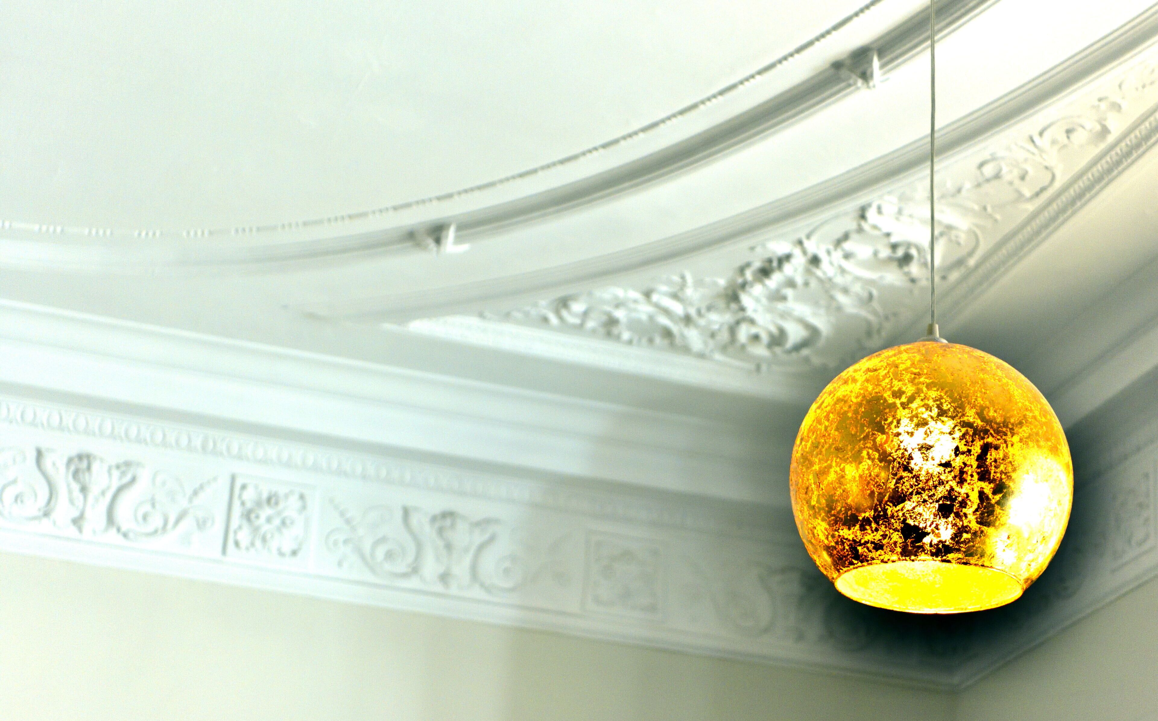 Una lámpara colgante esférica dorada suspendida de un techo blanco con molduras decorativas.