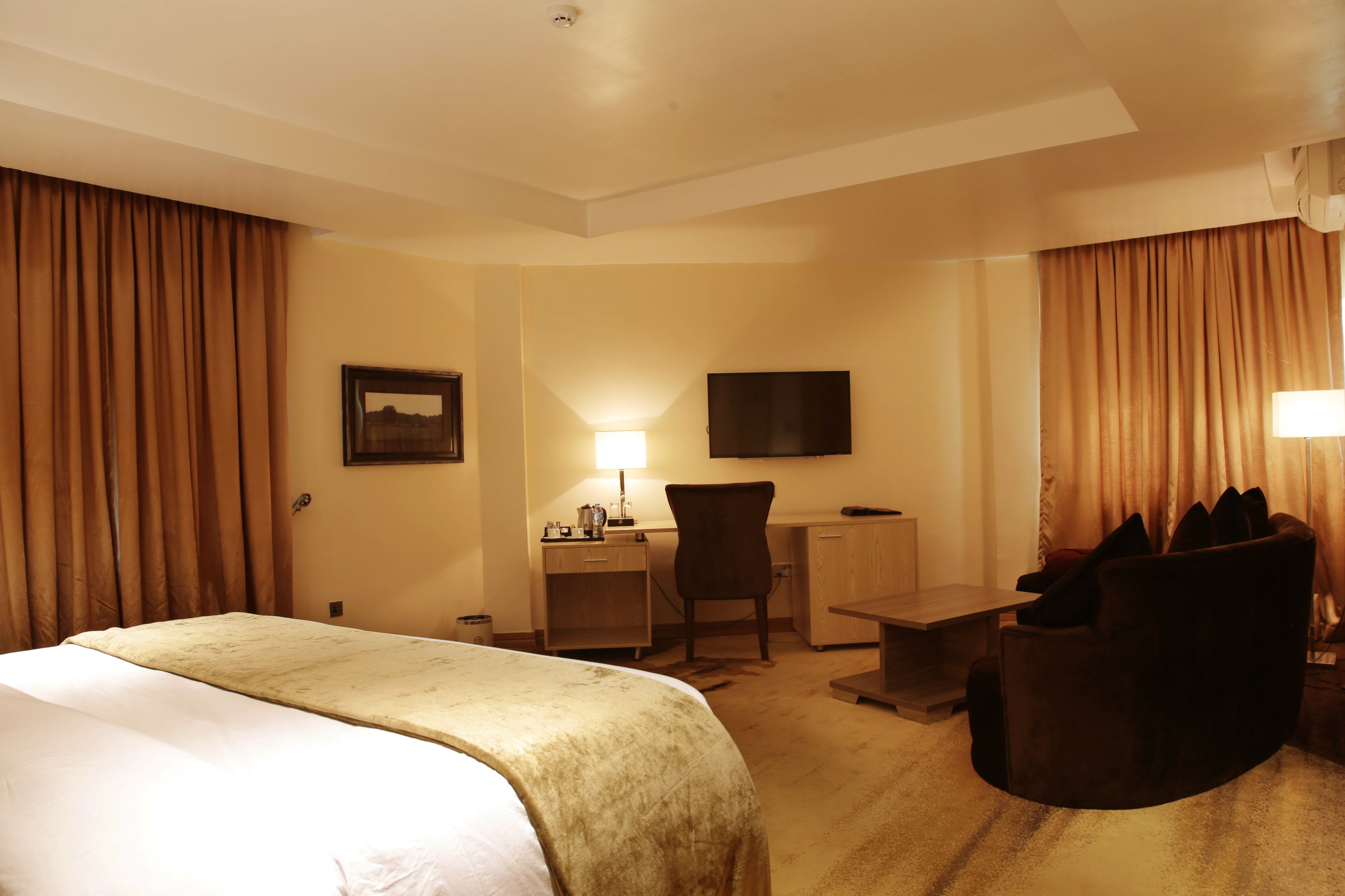 A hotel room with a large bed, a desk, a chair, and a TV mounted on the wall.