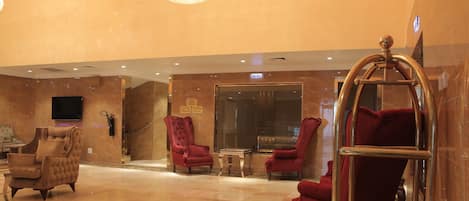 A lobby with marble flooring, red upholstered chairs, a chandelier, and a television mounted on the wall.