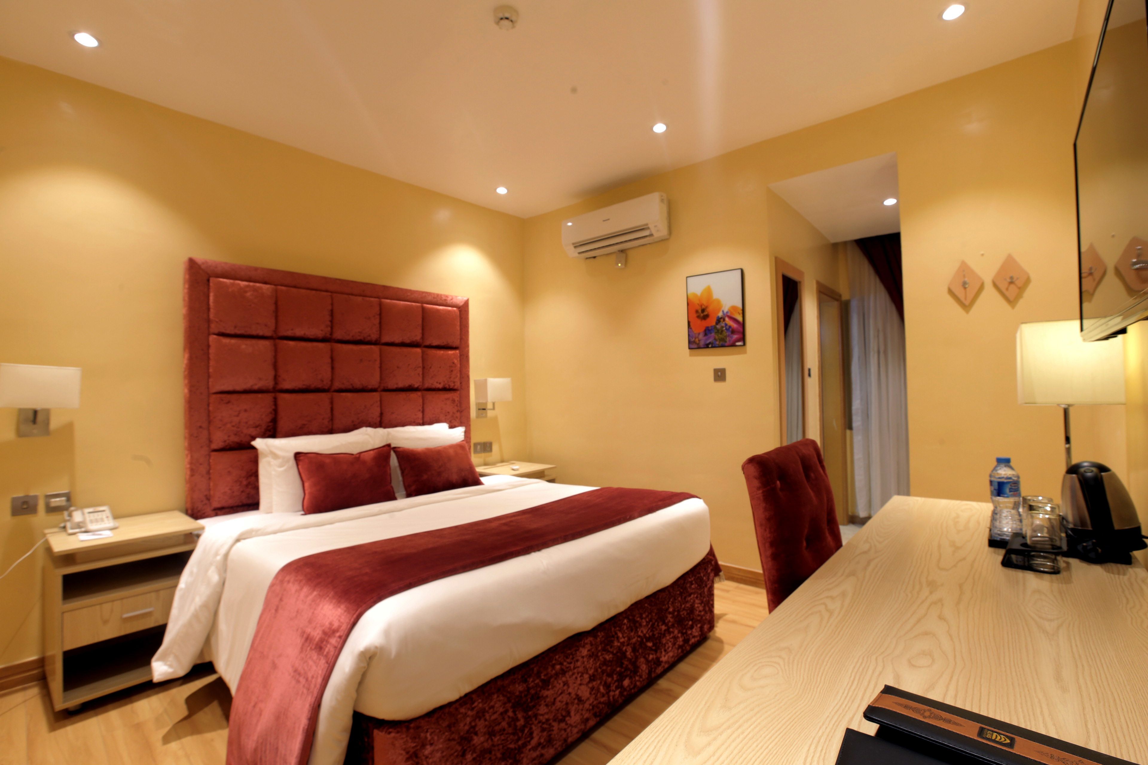 Una habitación de hotel con una cama grande, un escritorio de madera y una silla tapizada en rojo.
