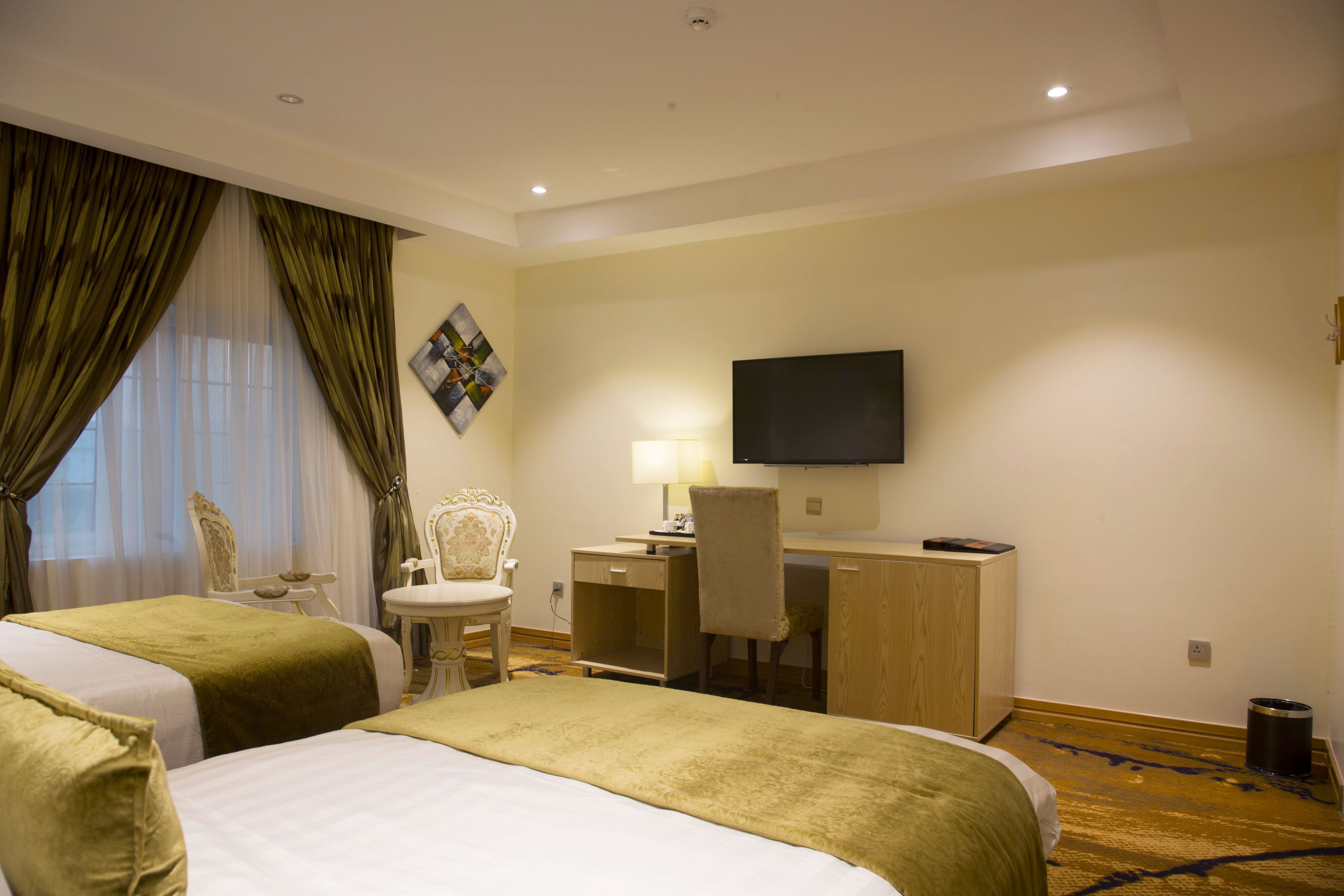 A hotel room with two beds, a desk, a chair, a television, and a painting on the wall.