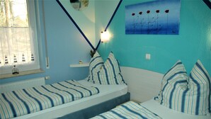 A room with two beds, each with striped bedding, a window with blinds, a wall-mounted light, and a painting of flowers. - Vacation cottage Albatros, Germany (Karlshagen)