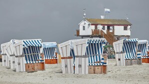 Sedie da spiaggia con rivestimenti a righe, una struttura in legno con tetto rosso e un edificio bianco con una bandiera.