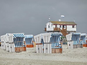 Strandstühle mit Streifen, eine Holzhütte mit rotem Dach und ein weißes Gebäude mit einer Flagge.