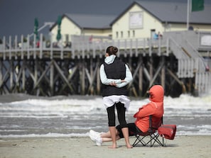A beach scene with a wooden pier and a building in the background.