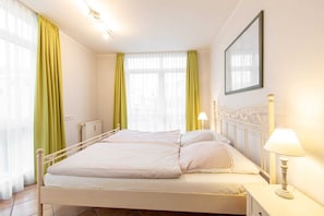 A neatly arranged bedroom with a bed, two bedside lamps, a radiator, and a framed picture on the wall.