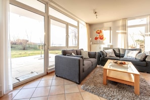 A spacious living room with a grey sofa, a wooden coffee table, and a large glass door leading to a patio.