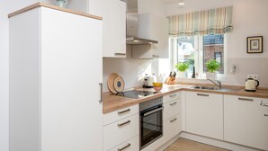 Una cucina moderna con mobili bianchi, un piano di lavoro in legno, forno integrato e una finestra con tenda a righe.