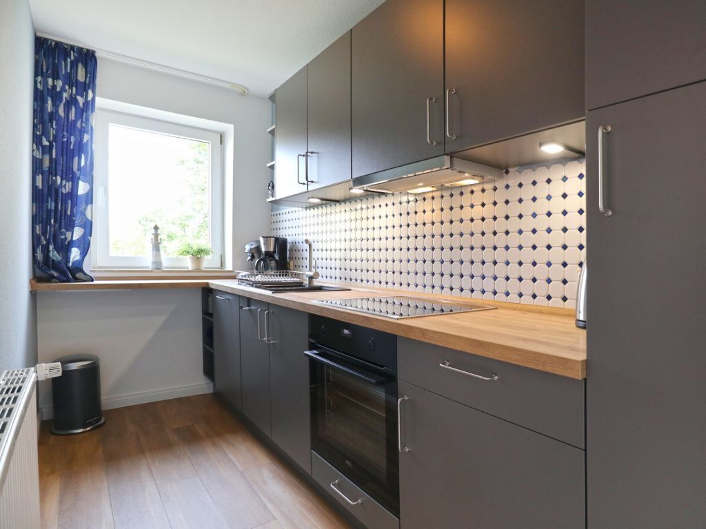 Una cocina moderna con gabinetes grises, encimera de madera y salpicadero de azulejos.