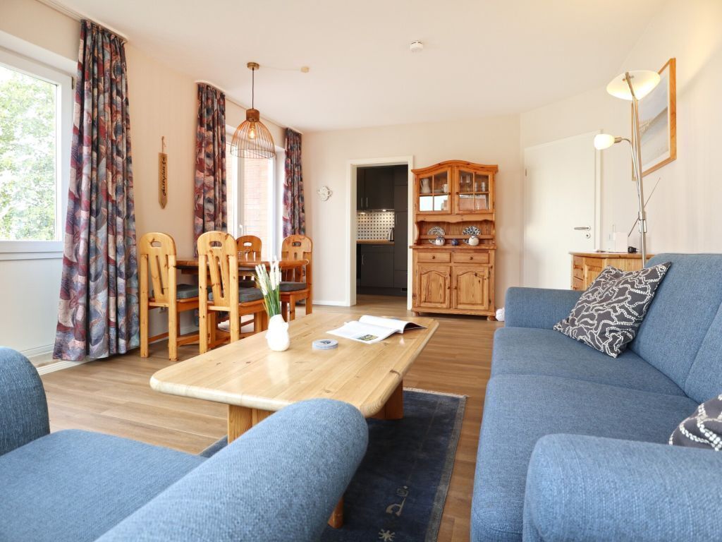 Ein Wohnzimmer mit einem blauen Sofa, einem Holzespeisetisch und Stühlen. Im Hintergrund ist eine Küche erkennbar.