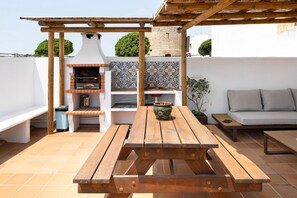 A wooden picnic table with benches, a grill, a tiled backsplash, and a sofa with cushions. - Holiday Home "Casa Boqueron" with Sea View, Rooftop Terraces and Wi-Fi (Conil de la Frontera)