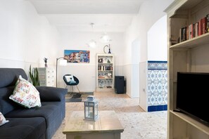 Una sala de estar con un sofá, una mesa de centro, una estantería, un televisor y una pared con estampado.