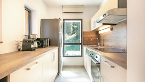 A modern kitchen with a wooden countertop, stainless steel appliances, and a window providing a view of greenery outside. - VVF Les 7 Laux Massif de Belledonne, Prapoutel (Les Adrets)
