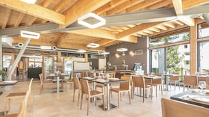 A spacious restaurant with wooden beams, modern lighting, and large windows offering views of the outside. - VVF Les 7 Laux Massif de Belledonne, Prapoutel (Les Adrets)