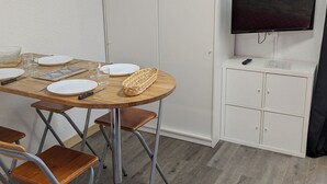 A room with a wooden dining table set for four, a television mounted on a cabinet, and a wardrobe with a mirror. - Cozy Studio for 4, Ski-In/Ski-Out, WiFi, Near Shops and Sports Center (Orcières Merlette)