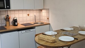 A compact kitchen with a dishwasher, a microwave, and a sink. There is a dining table with plates, glasses, and cutlery. - Cozy Studio for 4, Ski-In/Ski-Out, WiFi, Near Shops and Sports Center (Orcières Merlette)