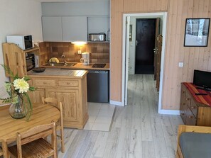 Une cuisine compacte avec un coin repas, des meubles de rangement en bois, un four à micro-ondes et une machine à café.