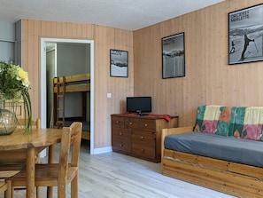 Une pièce chaleureuse avec un lit superposé, une commode en bois, un téléviseur et un canapé coloré.