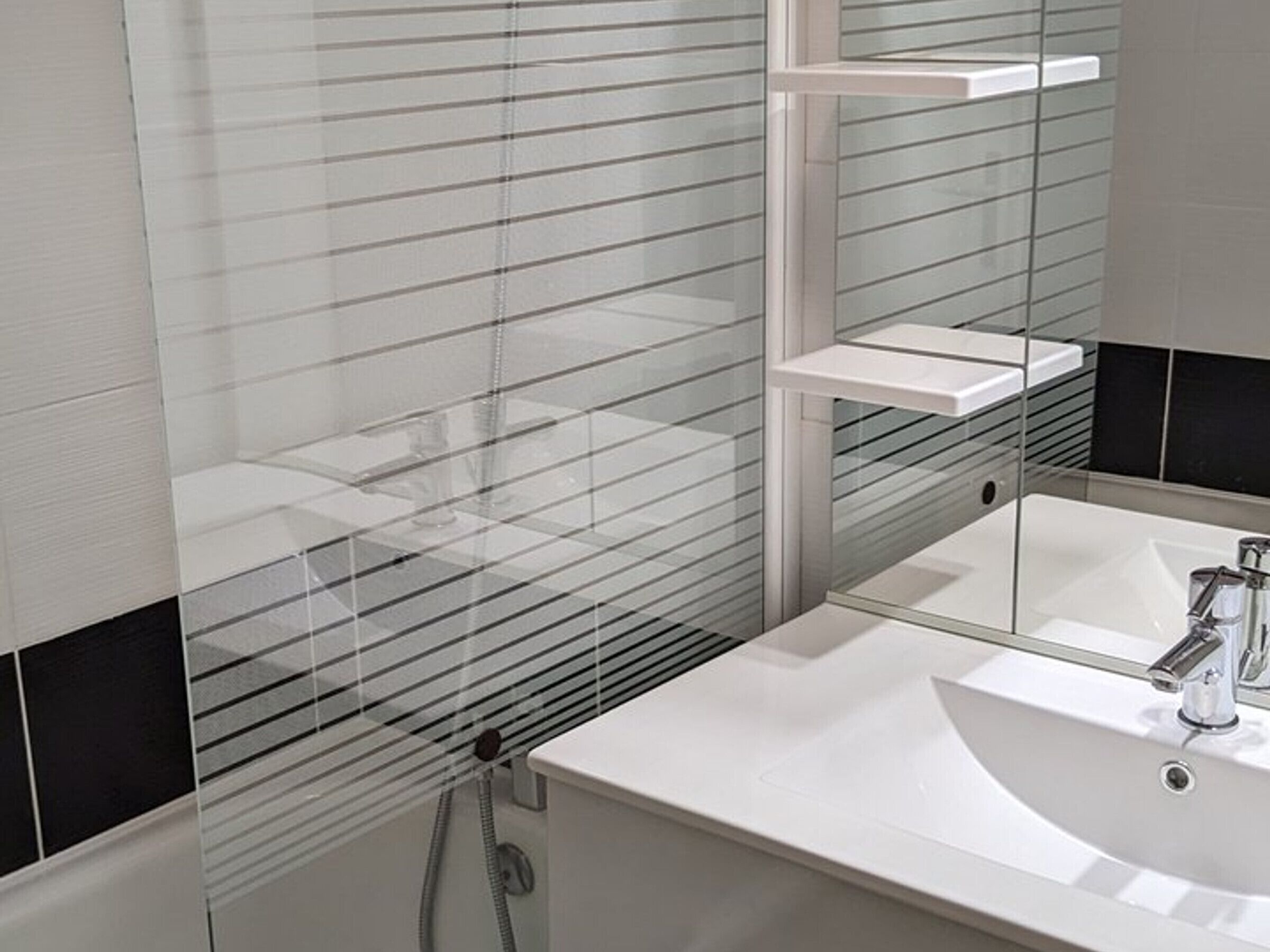 A modern bathroom with a white sink, a mirror, and a glass shower enclosure.