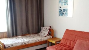 Ein kleines, gemütliches Zimmer mit einem Einzelbett, einem Holzstuhl, einem kleinen Tisch und einem roten Sofa.