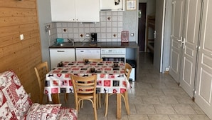 A compact kitchen with white cabinets, a dining table with a patterned tablecloth, and a wooden chair.