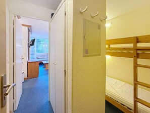 A room with a bunk bed, a door leading to another room, and a small window with a view of greenery outside.