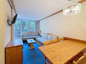 A room with a wooden table, a bench with cushions, a sofa, and a window with a view of trees.