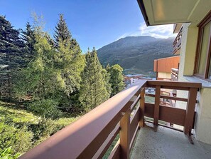 A balcony with a view of a mountainous landscape, trees, and buildings in the distance.