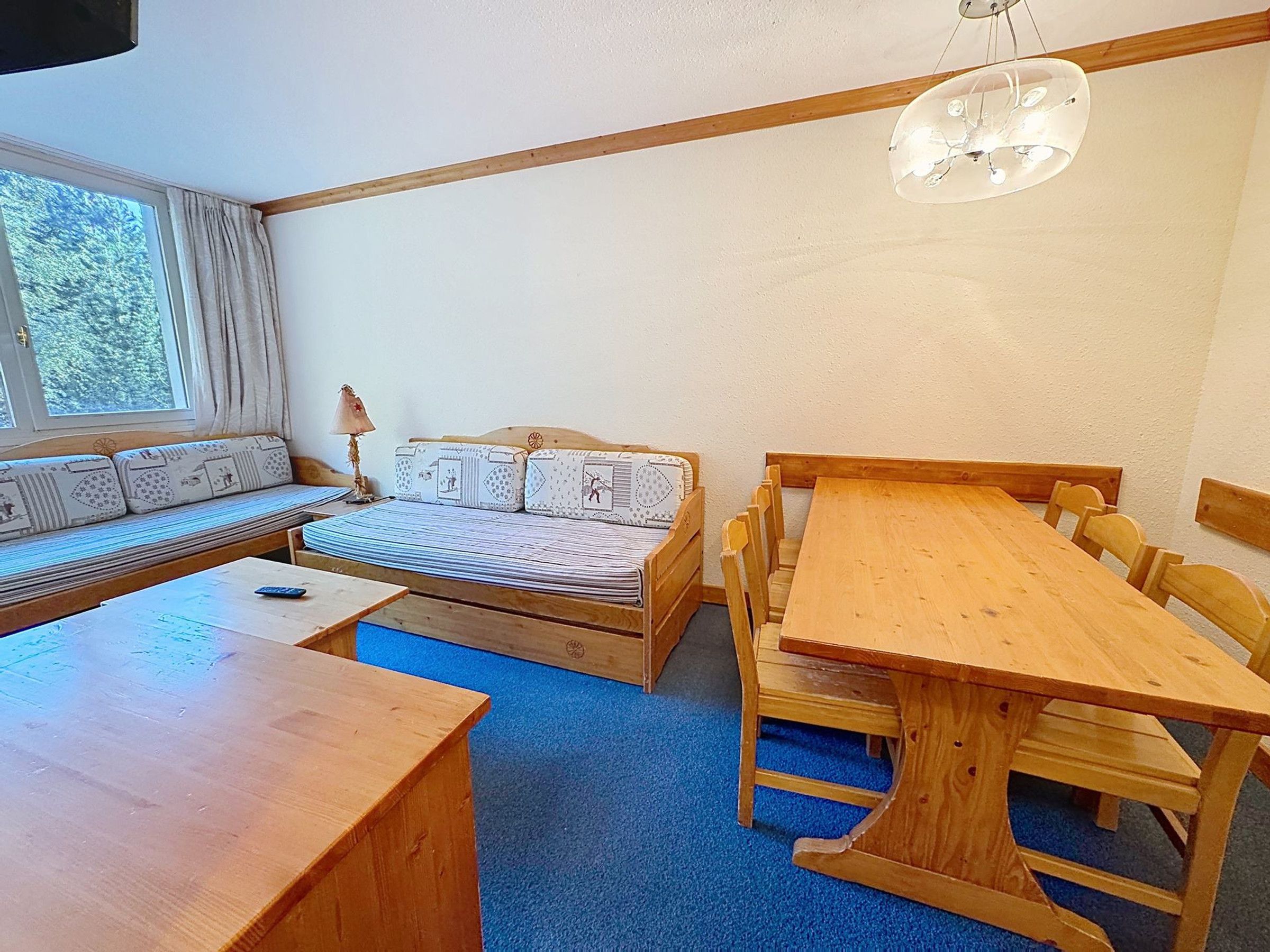 Una habitación acogedora con una mesa de madera, un sofá con cojines estampados y una ventana con cortinas.
