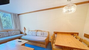 A cozy room with a wooden table, a sofa with patterned cushions, and a window with curtains.