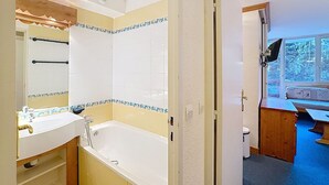 A bathroom with a bathtub, a sink, and a mirror. There is a window with a view of trees outside.