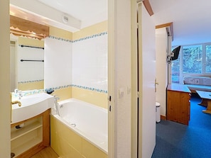 A bathroom with a bathtub, a sink, and a mirror. There is a window with a view of trees outside.