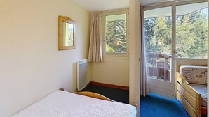 A bedroom with a single bed, a window with curtains, a radiator, and a view of greenery outside.