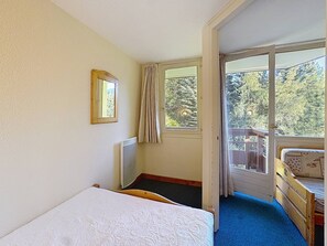 A bedroom with a single bed, a window with curtains, a radiator, and a view of greenery outside.
