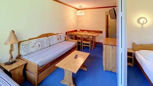 A compact room with a bed, a sofa, a dining table, and a small desk.