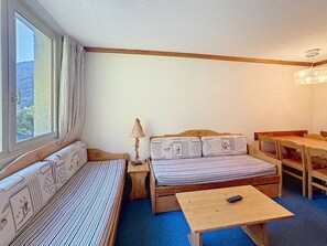 A small, cozy room with a bed, a table, and a chair. There is a window providing a view outside.