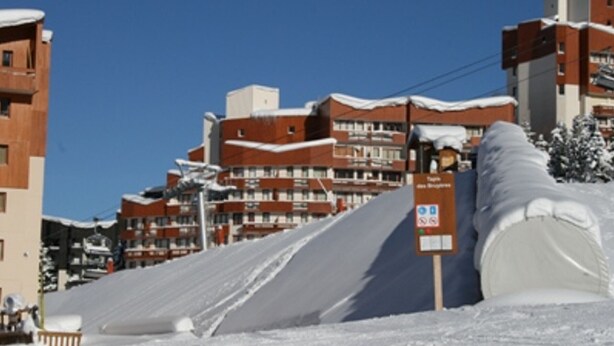 A snow-covered ski slope with buildings in the background.