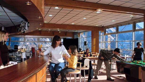 Un vaste espace intérieur comprenant une table de billard, un bar et de grandes fenêtres offrant une vue sur les montagnes.