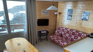 L’intérieur d’un chalet accueillant, avec une table à manger en bois, un canapé agrémenté de coussins à motifs, un téléviseur et une petite table d’appoint.