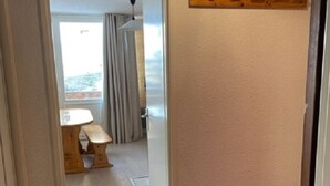 Un couloir avec un banc en bois, une porte et une vue sur une pièce où se trouvent une table et des rideaux.