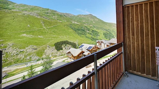 A balcony with a view of a mountainous landscape, wooden buildings, and a clear sky.